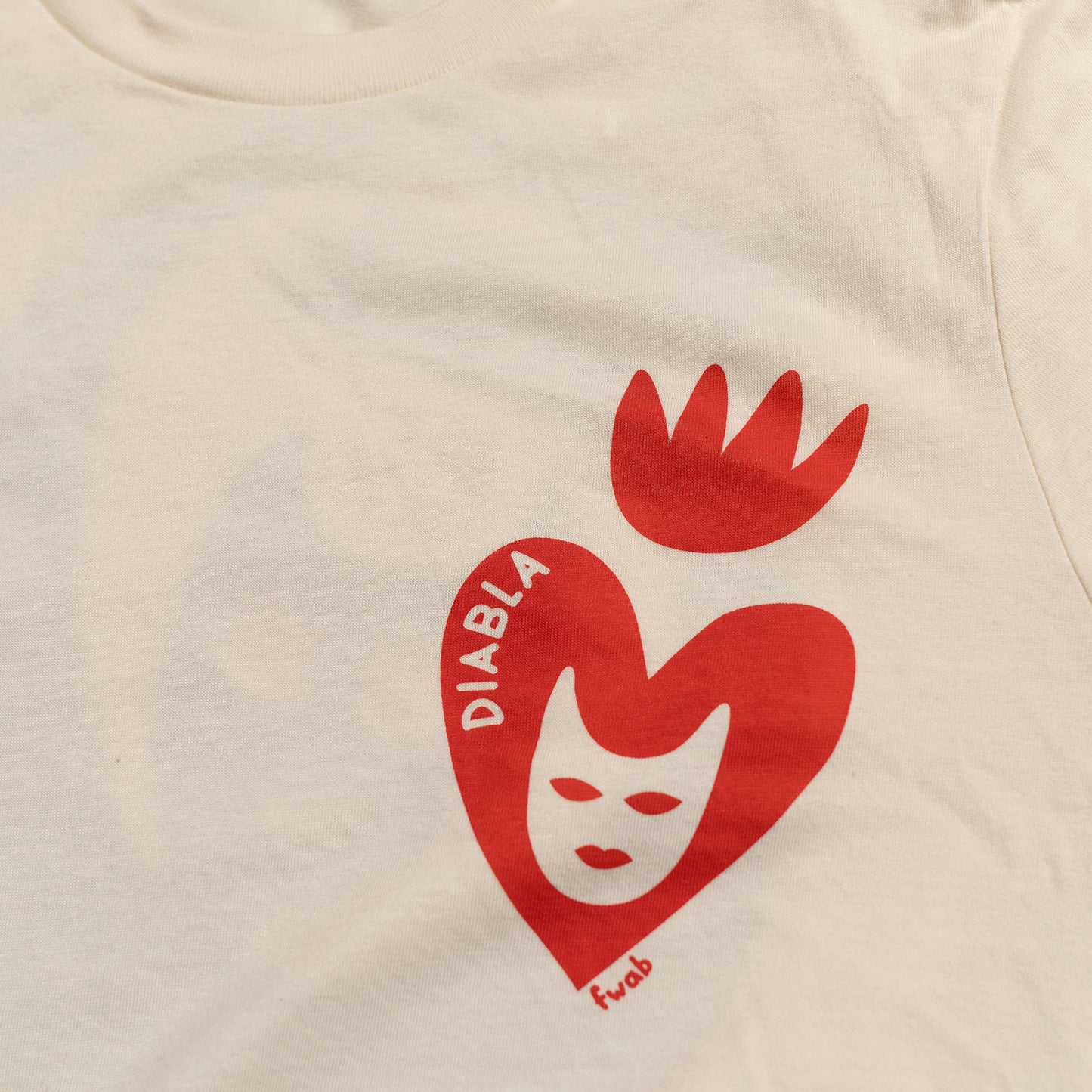 Closeup detail of print graphic on front side of shirt. heart with fire crown and inside devil face and the word "diabla"